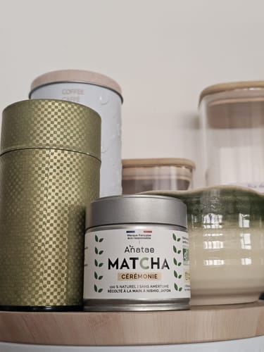 Le Matcha Cérémonie d'un client dans sa boîte argentée, sur une étagère en bois parmi d'autres récipients.