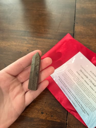 Reviewer holding a small, dark Hematite crystal tower from their monthly subscription over a wooden table.