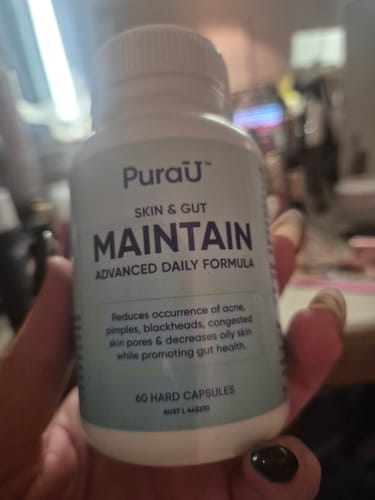 Customer holding a white bottle of the Skin & Gut Maintain™ supplement.