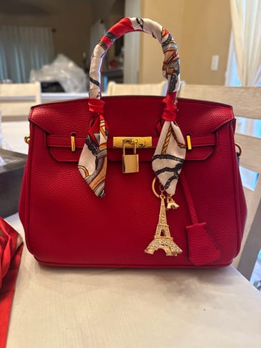 Customer's red Warkin Bag on a table, styled with a scarf on the handle and an Eiffel Tower charm.