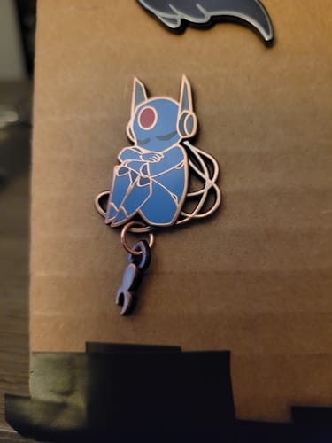 Close-up of the reviewer's blue and copper Waxing Moondown Pin attached to its cardboard backing.