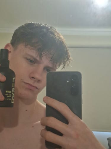 Reviewer in a mirror selfie holds the Beachy Flow Duo spray, showing off their textured hairstyle after use.