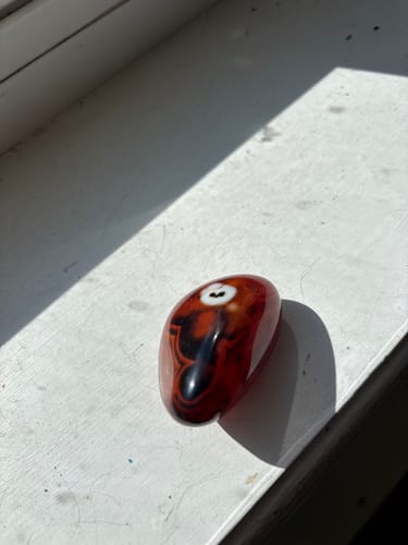 Customer's polished monthly crystal, a reddish-brown stone with black swirls, sitting on a sunny windowsill.