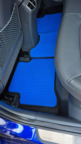 Recenzent pokazuje niebieskie, dopasowane dywaniki na zamówienie na tylnym siedzeniu samochodu.