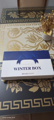 Customer shows the ZING Scents Winter Box with its decorative blue and white sleeve on a patterned table.