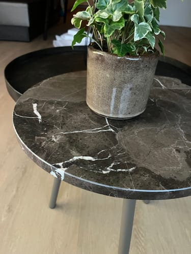 Klant toont een close-up van de Vein bijzettafel met donker marmeren blad en een plant erop.