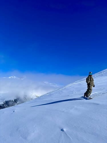 Reviewer wearing baggy khaki corduroy snow pants while snowboarding down a snowy mountain slope.