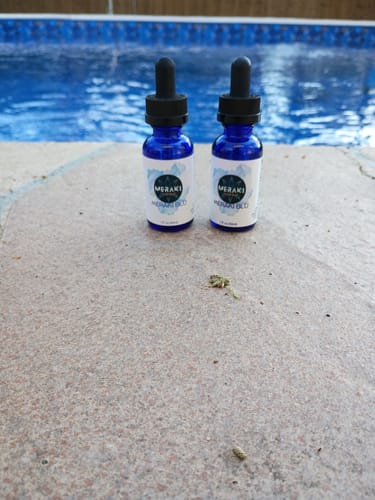 Reviewer's two Meraki Blu Methylene Blue dropper bottles on a stone ledge next to a pool.