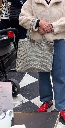 Customer holding the woven Cruiser Neoprene Tote Bag in sage green, styled with a cream coat and blue jeans.
