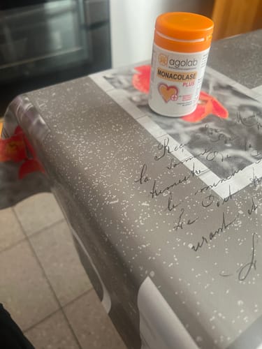 Il cliente mostra il flacone di Monacolase PLUS con il tappo arancione, appoggiato su un tavolo.