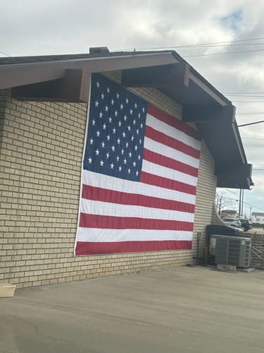Reviewer's large, heavy-duty American flag displayed vertically on the side of a brick building.