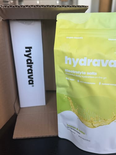 Reviewer unboxing hydrava electrolyte salts, showing the lime-green Lemon & Lime pouch and its white box.
