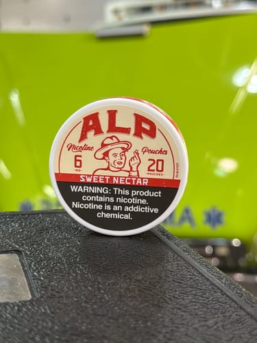 Customer's close-up of a white and red can of ALP 6mg Nicotine Pouches on a textured surface.