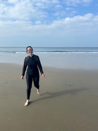 Reviewer smiling on a beach while wearing the long-sleeve Swim Top Full Zip and matching leggings.