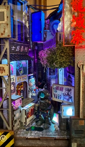 Customer's assembled Kowloon Walled City 2049 Book Nook Kit lit by deep blue and purple lights with a custom robot figure.