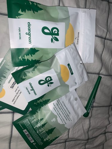 Customer's several 'cleangreen' branded pouches of cannabis products on a bed.