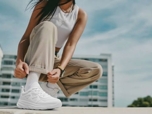 Customer wearing the white Motion X sneakers while squatting outdoors on a sunny day.