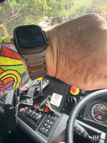 A customer's wrist wearing the WatchBand Titanium Sport with orange accents, shown inside a vehicle.