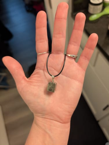 Reviewer's hand holding the square-shaped monthly crystal on a black necklace cord.