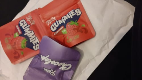 Customer's purple packet of ROLLZ - Chocolope THC Chocolate alongside two red packets of gummies on a white surface.