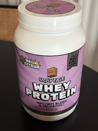 Customer's white tub of UGLYFACE WHEY PROTEIN in the Vanilla Ice Cream flavor on a dark surface.