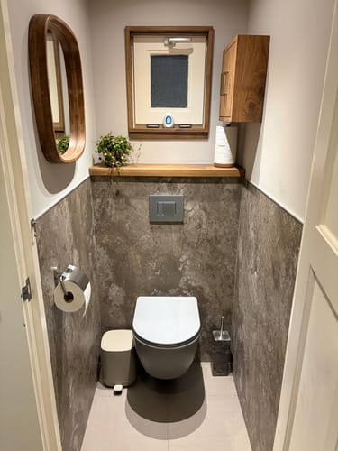 Recensent toont de by fonQ Pane spiegel met een houten rand, opgehangen in een toiletruimte.