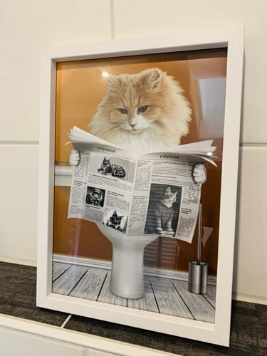 Kunde zeigt das lustige Poster 'Wichtige Sitzung' in einem weißen Rahmen, das in einem Badezimmer aufgestellt ist.