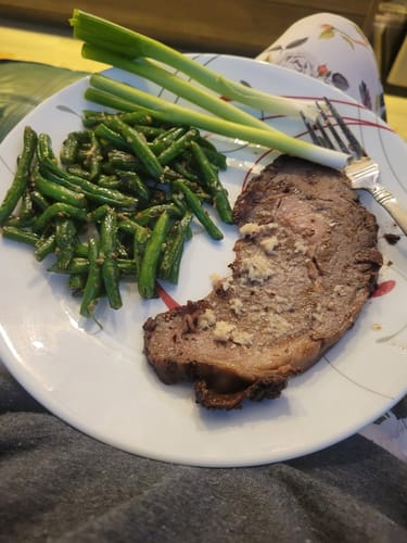 Customer's meal featuring a slice of Pre-Cooked Smoked Prime Rib with seasoned green beans and green onions on a plate.
