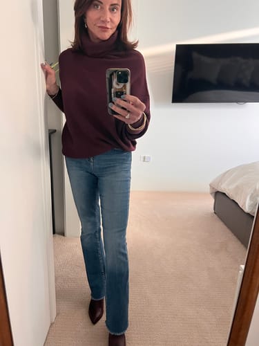 Reviewer in a mirror selfie showing the fit of the plum Asymmetric Draped Roll Neck sweater with jeans.