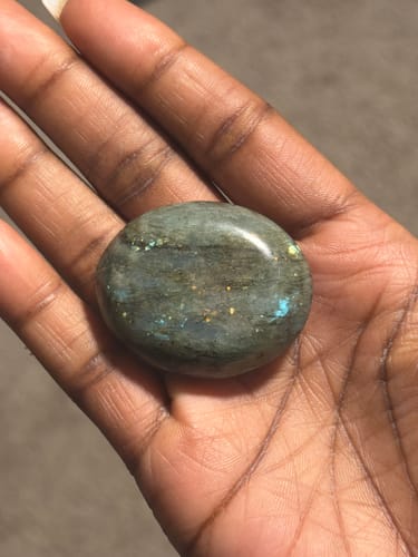 Customer holding a polished, iridescent labradorite crystal in their open palm.