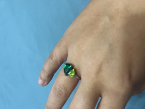 A customer's hand wearing the Leesha Birthstone Ring with two different green, pear-cut stones on a silver band.