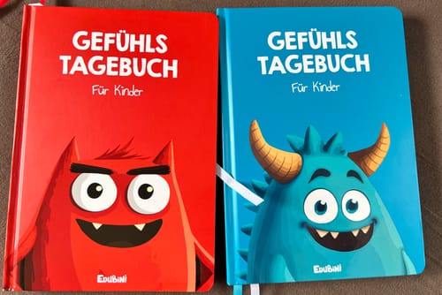 Rezensent zeigt zwei Gefühlstagebücher für Kinder, eines in Rot und eines in Blau, mit Monster-Illustrationen.