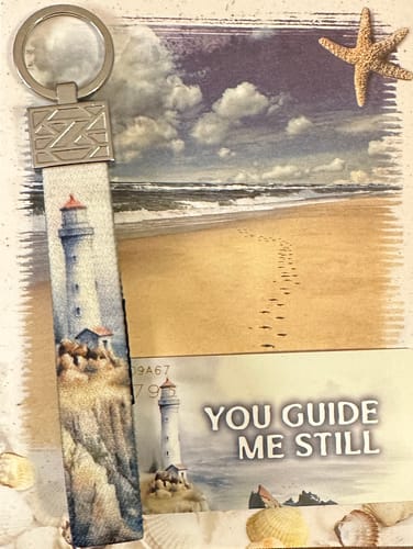 Reviewer's You Guide Me Still Bracelet with a lighthouse design, shown with its matching collector's card and seashells.