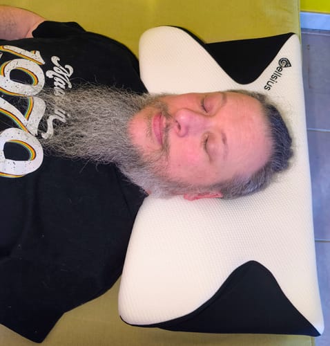 Client allongé sur le dos, la tête reposant sur un coussin cervical orthopédique bicolore.