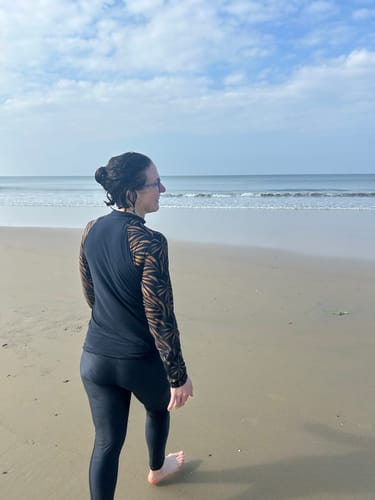 Reviewer from behind wearing black Swim Leggings and a matching top while walking on a sandy beach.