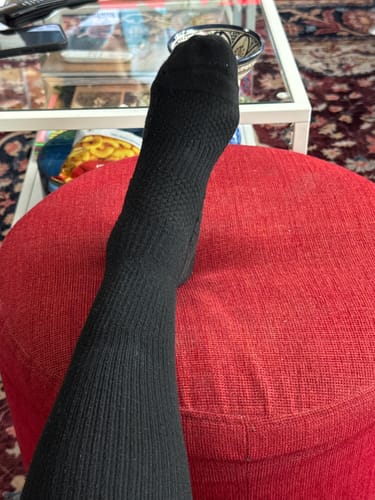 Recensentens fot med en svart Diasocks stödstrumpa som vilar på en röd fotpall.