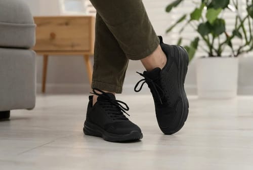 Customer wearing the all-black Balance Pro sneakers indoors with their ankles crossed.