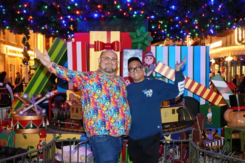 Reviewer wearing the colorful 'The Scare Floor' Performance Hoodie in front of a festive holiday display.