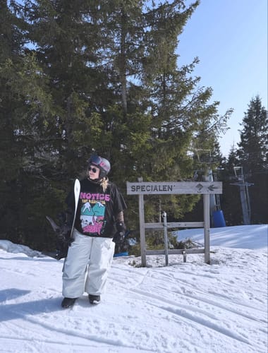 Reviewer wearing the baggy snow pants while holding a snowboard on a snowy mountain.