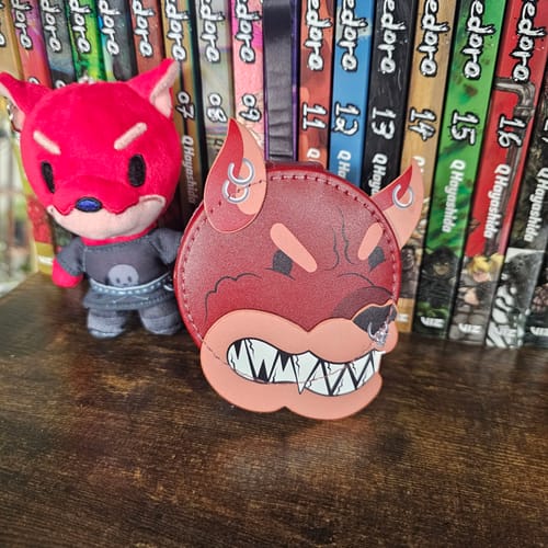 Reviewer's red Hellhound Travel Case on a wooden shelf in front of a row of manga.