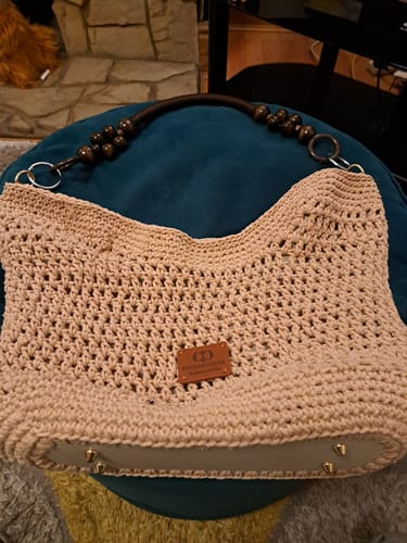 Customer's completed beige Sunny Beach Tote with a beaded handle, sitting on a dark teal cushion.