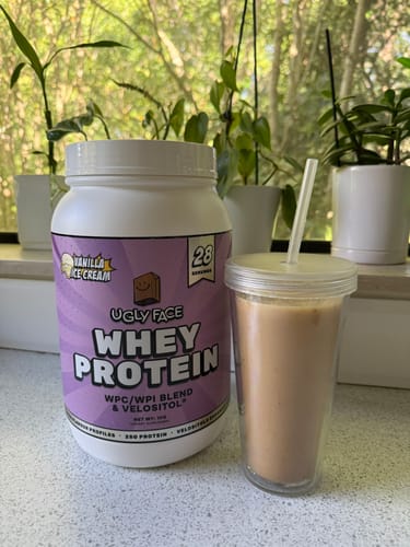 Customer's tub of UGLYFACE WHEY PROTEIN, Vanilla Ice Cream flavor, on a counter next to a tumbler of iced protein coffee.