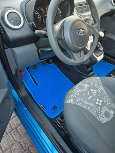 Recenzent pokazuje niebieski dywanik samochodowy Micro, idealnie dopasowany do podłogi po stronie kierowcy.