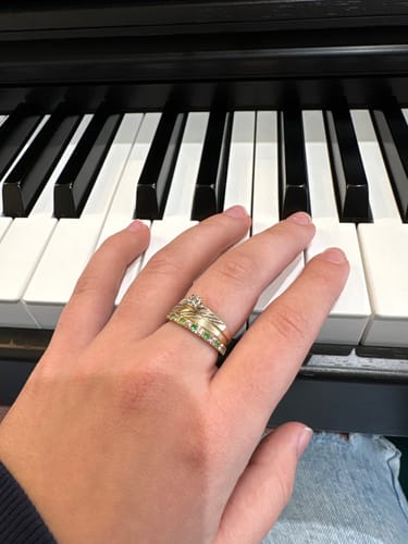A customer's hand on piano keys wearing the gold Eterna Birthstone Ring with green stones, stacked with another ring.