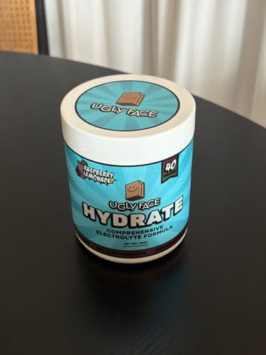 Customer's tub of UGLYFACE HYDRATE in Raspberry Lemonade flavor sitting on a black table.