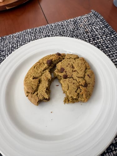 Reviewer's Cael's Chocolate Chip Cookie broken in half on a white plate, showing its soft texture.