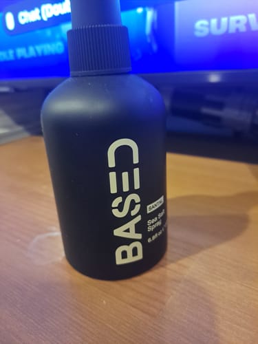 Customer's black bottle of Based Bodyworks Sea Salt Spray sitting on a wooden table.