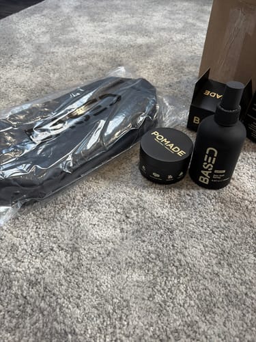 Customer's Beachy Flow Duo sea salt spray and pomade with a black toiletry bag on a grey carpet.