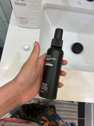 Customer holding the black Skin Revival Spray bottle in a bathroom setting.