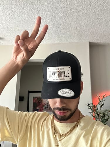 Customer wearing a black Puerto Rico Plate Hat with a custom 'TOMMY ROYALE' patch, making a peace sign.